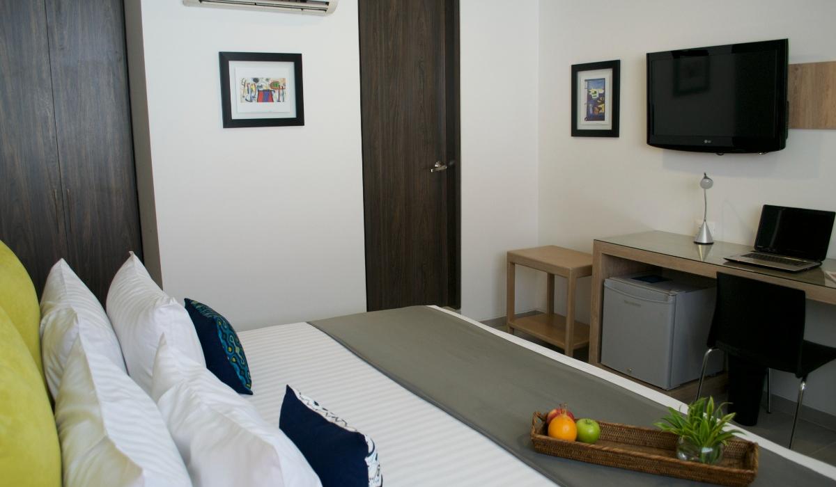 Habitación moderna con cama cómoda y decoración elegante en Hotel Casablanca Cúcuta. Habitación de hotel con cama doble, cojines coloridos, TV, escritorio y aire acondicionado.