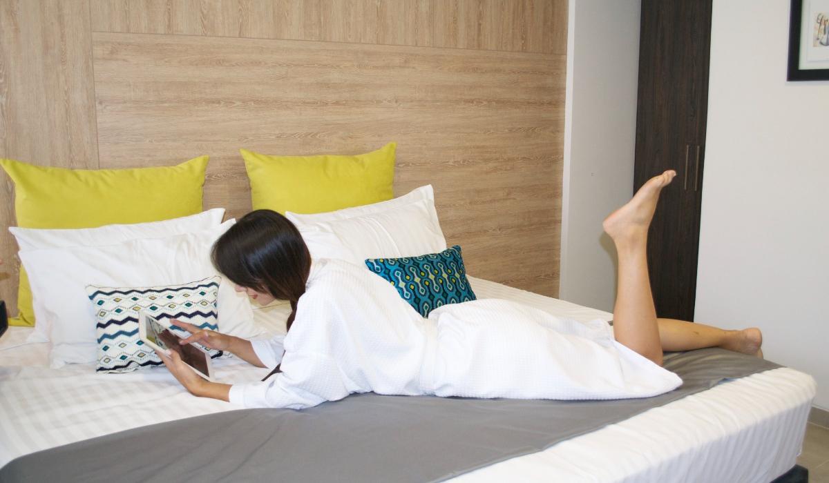Relajación en habitación moderna del Hotel Casablanca Cúcuta. Persona usando tablet en cama de hotel con cojines coloridos y cabecera de madera en Cúcuta.