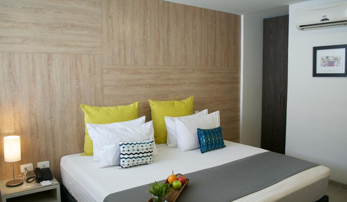 Habitación moderna con cama cómoda y decoración elegante en Hotel Casablanca Cúcuta. Habitación moderna con cama doble, cojines coloridos y bandeja con frutas en Hotel Casablanca Cúcuta