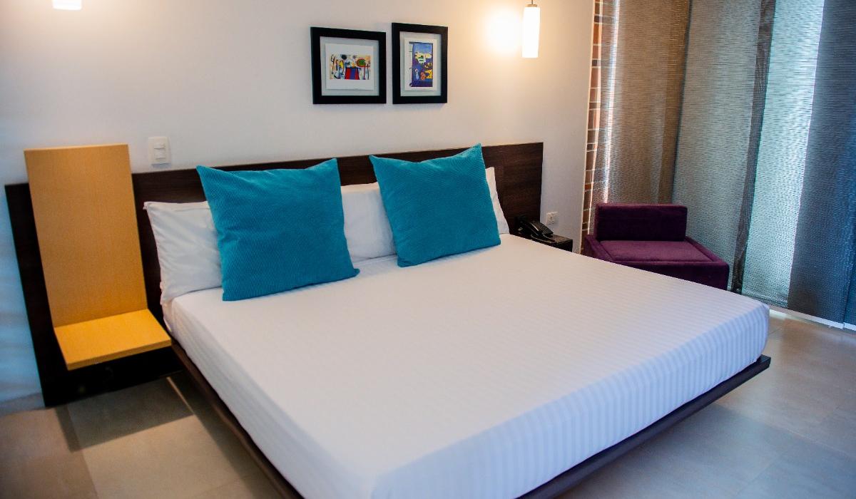 Habitación moderna con cama matrimonial y decoración elegante en Hotel Casablanca Cúcuta. Habitación moderna con cama matrimonial, cojines azules y decoración minimalista en hotel de Cúcuta.