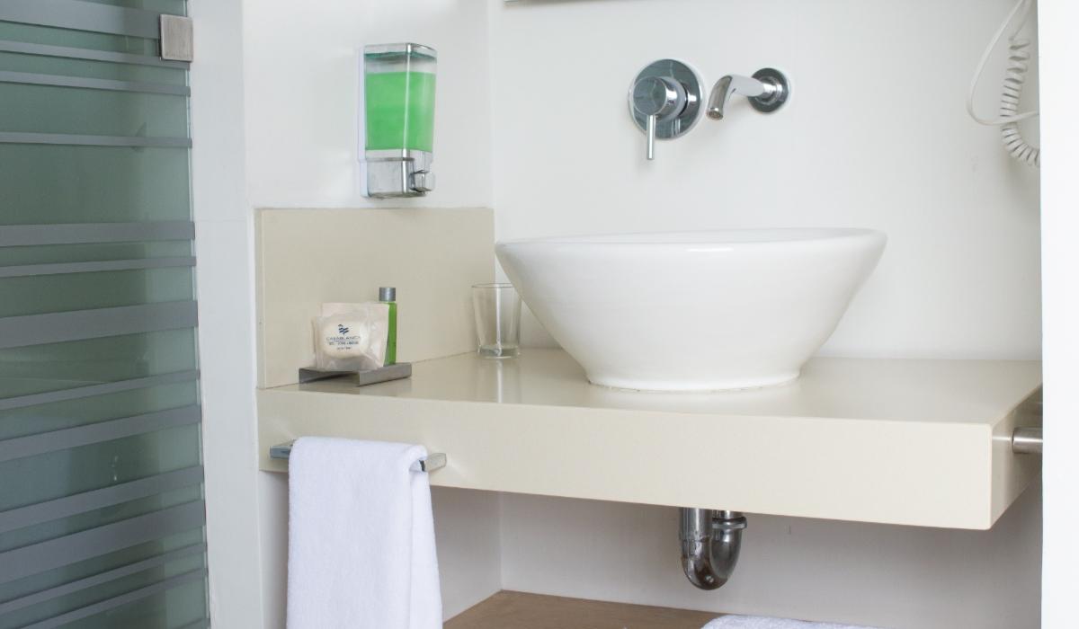 Baño moderno con lavabo y accesorios básicos en Hotel Casablanca Cúcuta. Baño moderno con lavabo elegante, dispensador verde y toalla blanca en Hotel Casablanca Cúcuta.