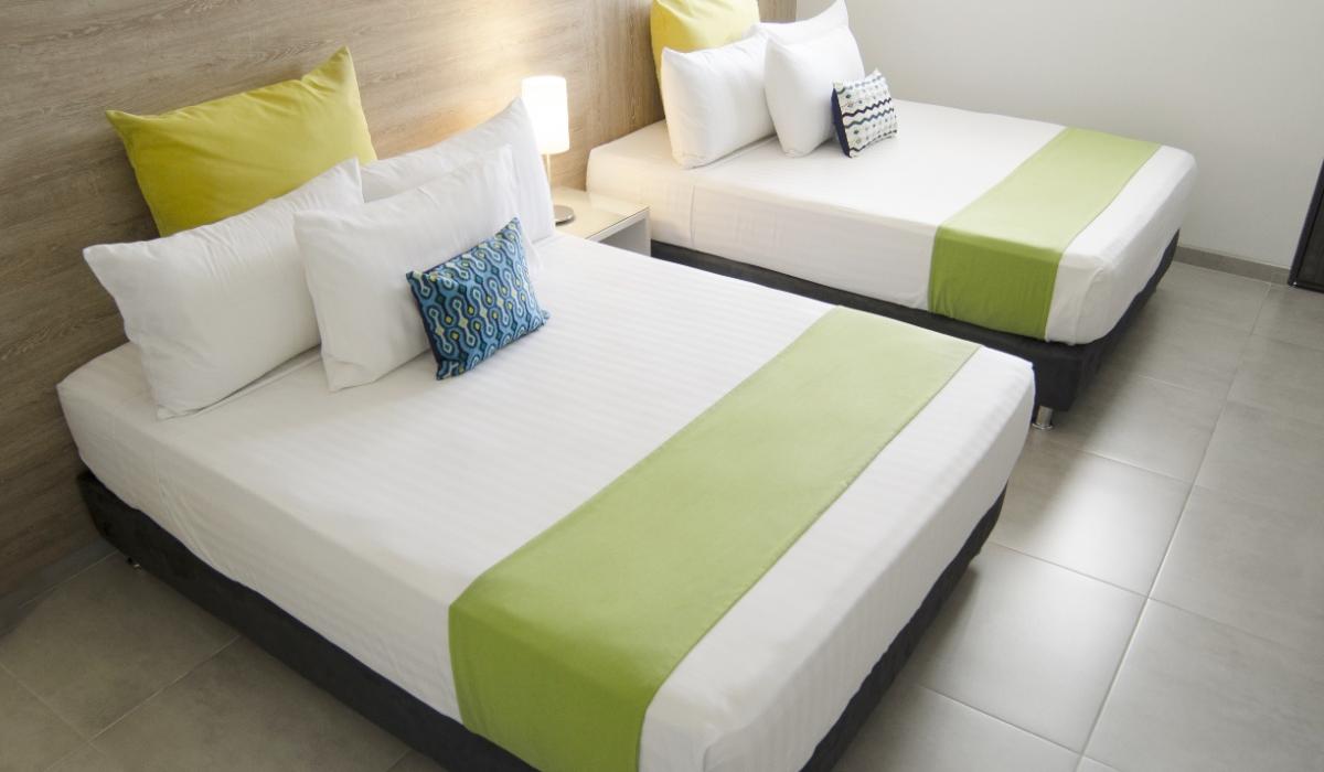 Habitación doble con decoración en tonos verdes y azules en Hotel Casablanca Cúcuta. Dos camas dobles con almohadas verdes y cojines azules en habitación del Hotel Casablanca Cúcuta.