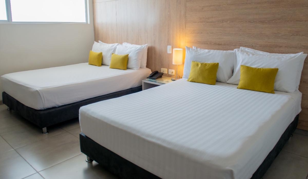 Habitación moderna con dos camas dobles y decoración minimalista en Hotel Casablanca Cúcuta. Habitación con dos camas dobles, almohadas amarillas y lámpara de noche encendida en hotel de Cúcuta