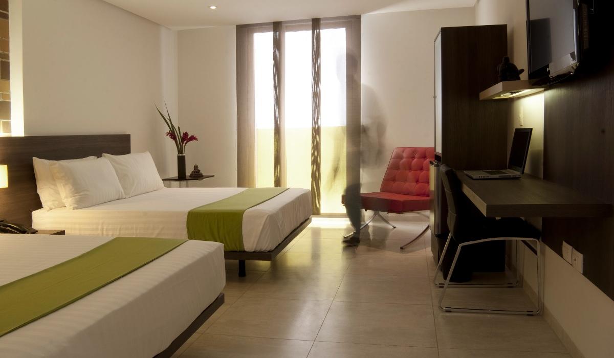 Habitación moderna con dos camas dobles y escritorio en Hotel Casablanca Cúcuta. Habitación moderna con dos camas dobles, escritorio y silla roja en hotel de Cúcuta