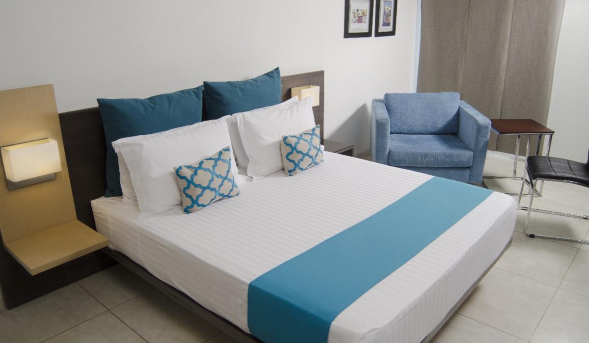 Habitación doble con decoración elegante en Hotel Casablanca Cúcuta. Habitación doble moderna con cojines azules y silla cómoda en Hotel Casablanca Cúcuta.